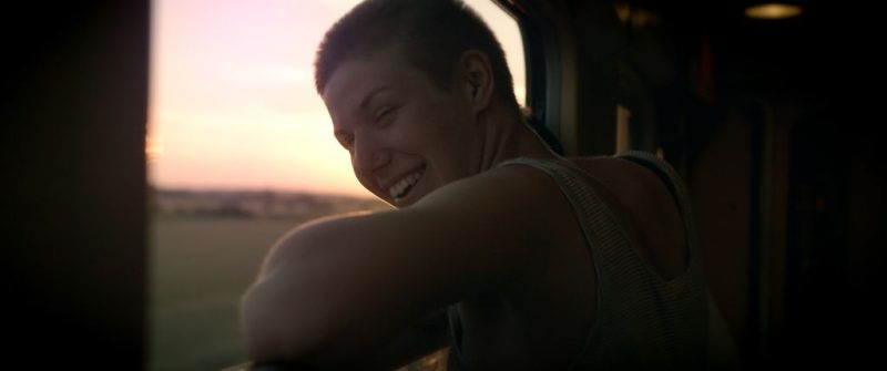 Uśmiechnieta młoda kobieta wychyla się przez okno stojąc na korytarzu w pociągu