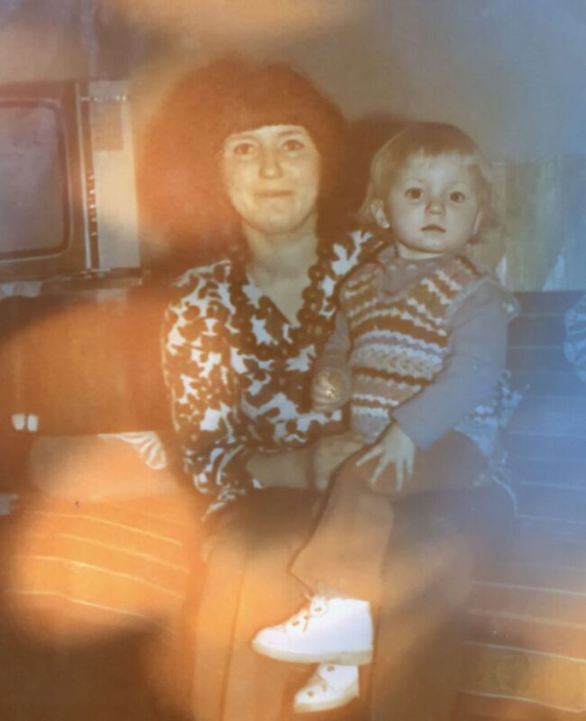 Kobieta siedzi na kanapie w pokoju i trzyma na kolanach małe ok. 3 letnie dziecko.