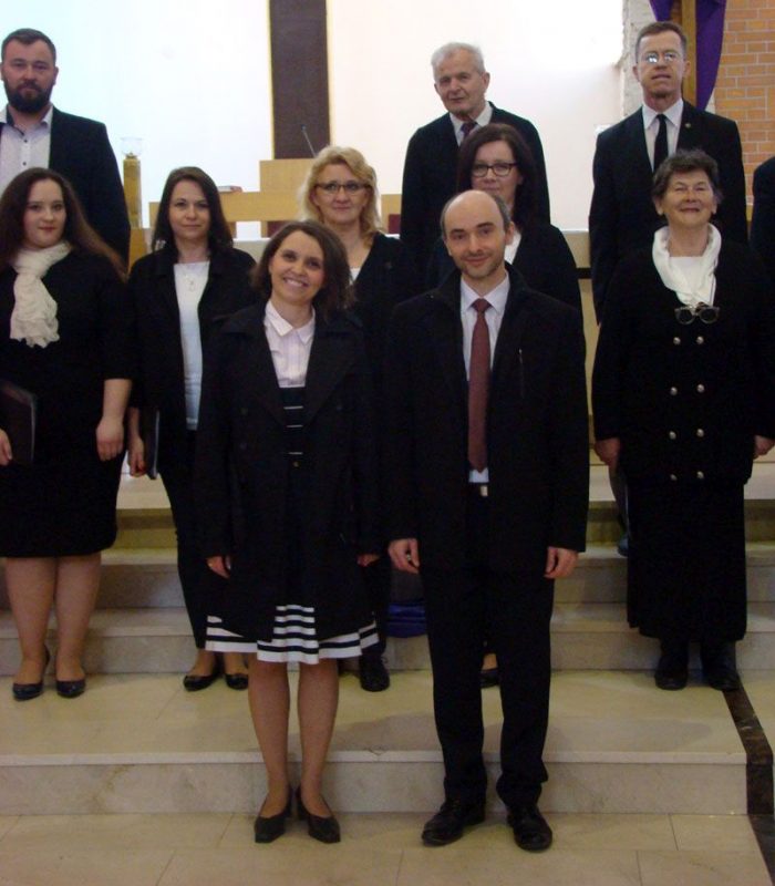 Grupa dorosłych osób ubranych w galowe stroje stoi na schodach w kościele
