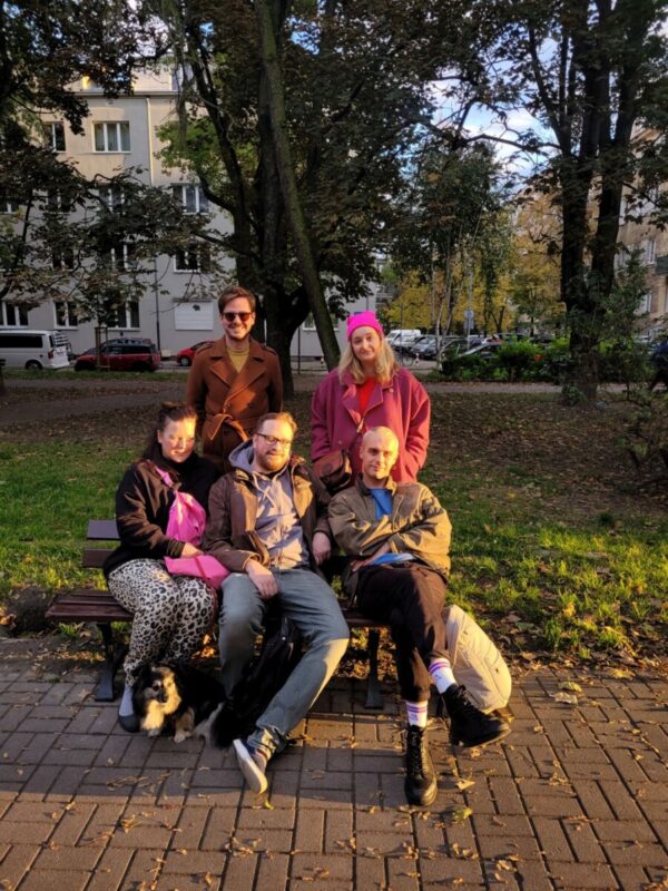 Pięcioro dorosłych (3 kobiety, dwoje mężczyzn) siedzi w parku na ławce.
