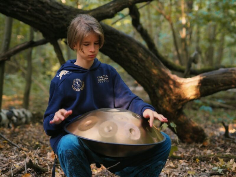 Nastolatek znajduje się w lesie i gra na handpanie.