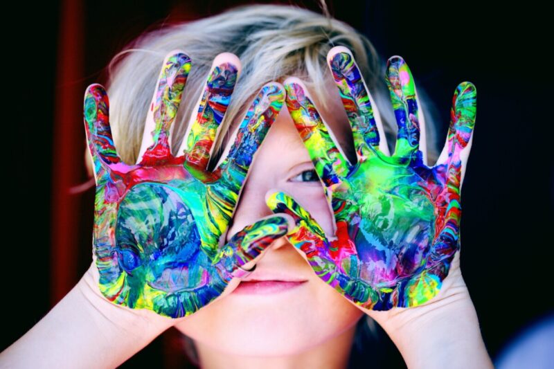 Dziecko, które ma umazane farbami obie ręce od wewnętrznej strony, podnosi je do góry.