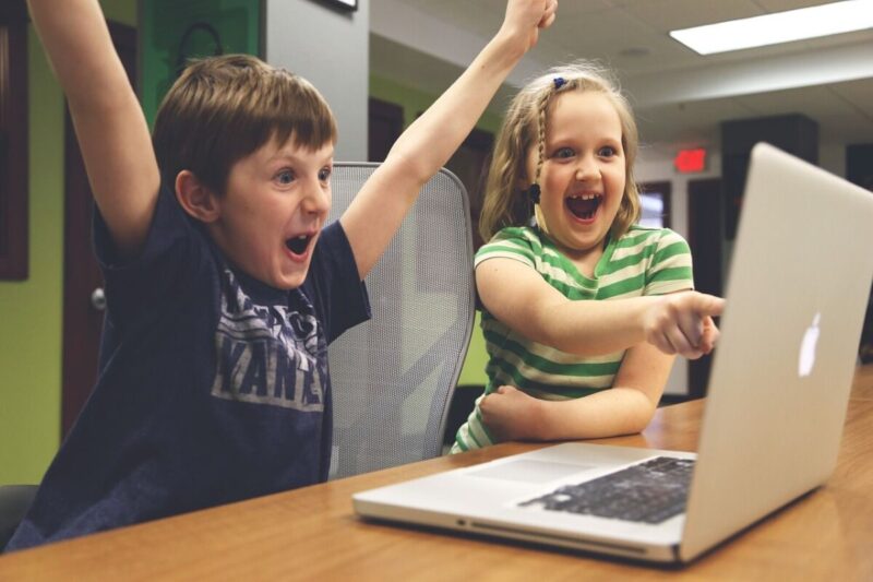 Dwoje chłopców siedzi przed laptopem, oboje cieszą się najprawdopodobniej na dobrze wykonanie zadanie, które zlecił im instruktor