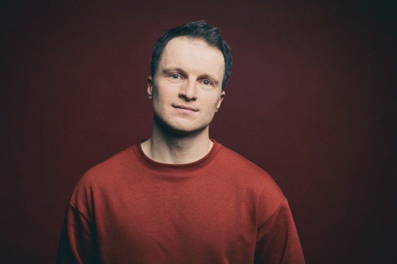 Mężczyzna w czerwonej bluzie, na ciemnym tle.