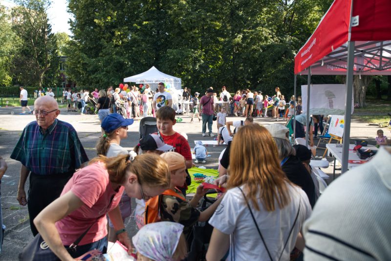 Na terenie boiska szkolnego znajdują się stoiska w namiotach. Przy stoiskach sporo dzieci z rodzicami.